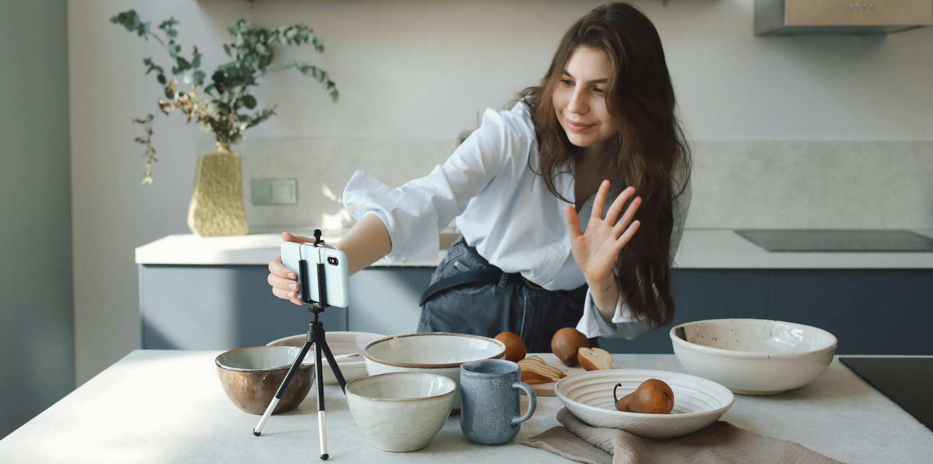 Woman influencer in kitchen recording waving to phone camera