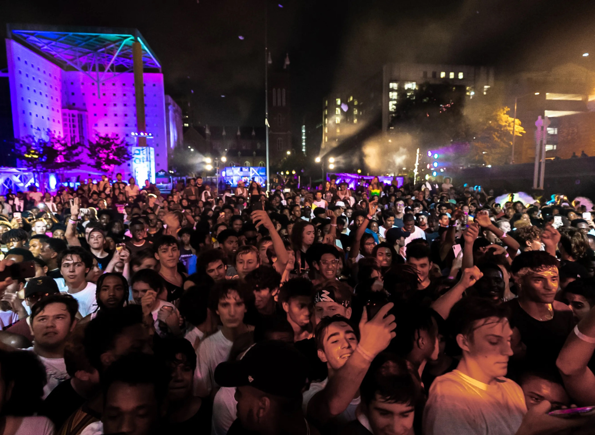A dense nighttime crowd stands facing a brightly lit stage at an outdoor Destination Atlanta event.