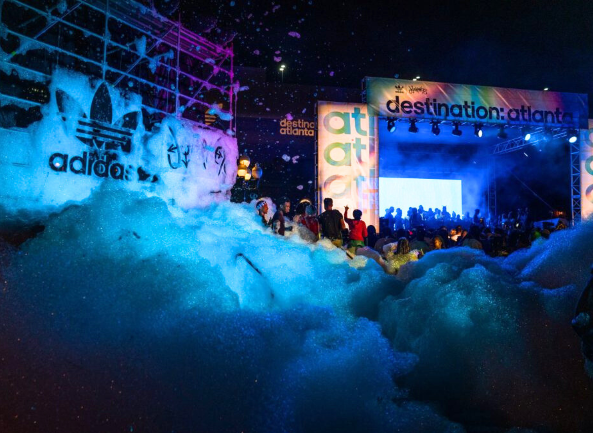 A nighttime outdoor event with foam covering the crowd in front of a brightly lit Destination Atlanta stage.