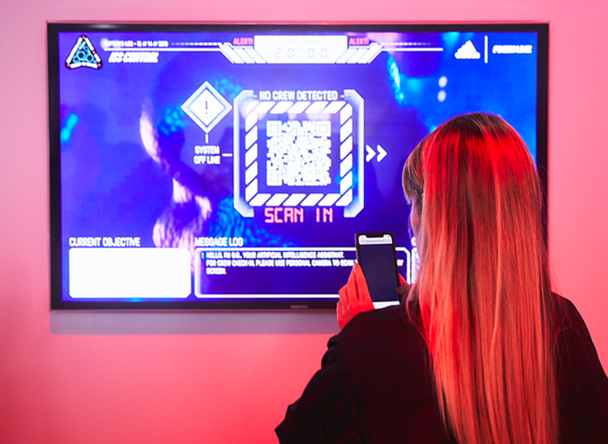 Guest scans a QR code on a digital screen as part of the Goodbye Gravity interactive experience.