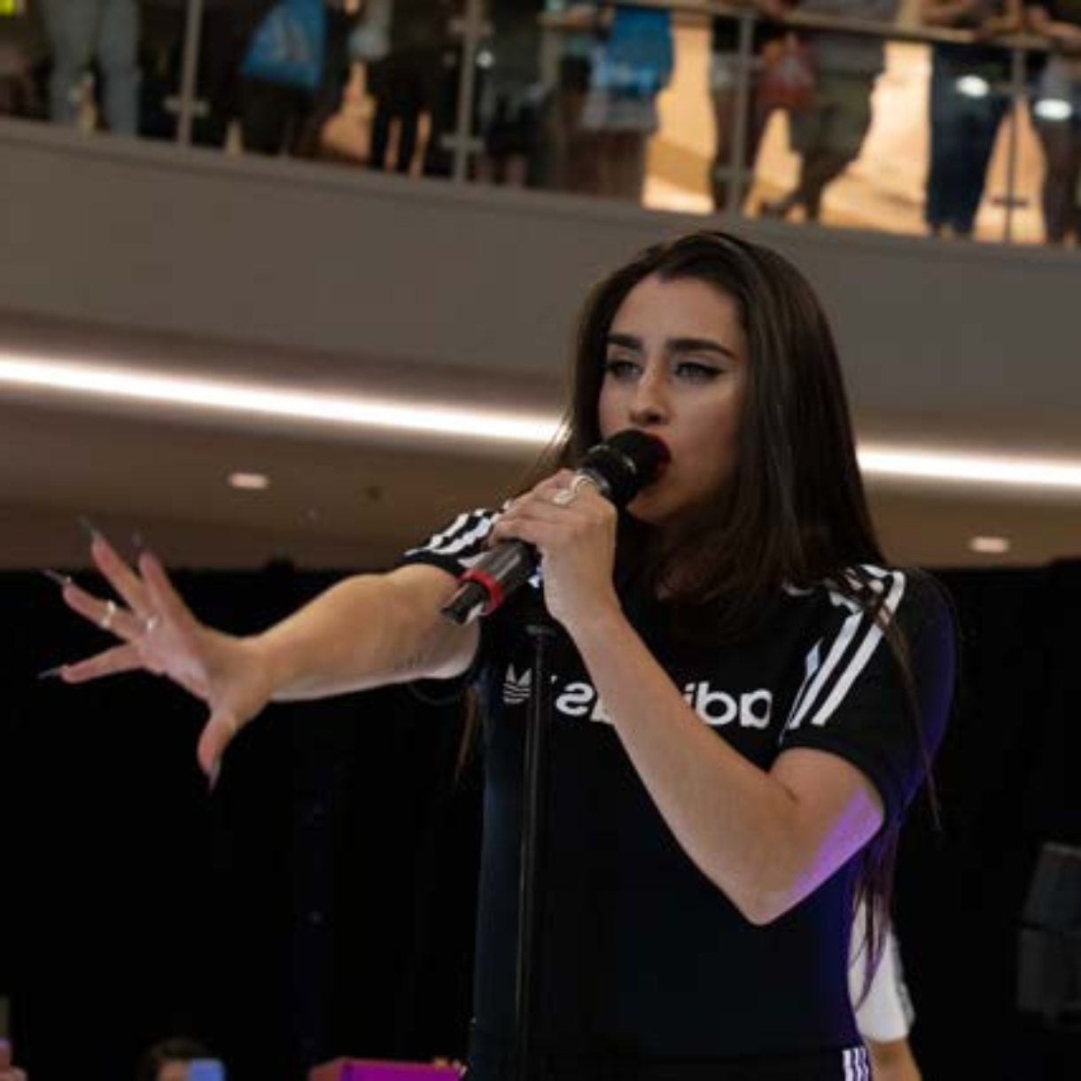 Featured artist performing live on stage wearing an adidas outfit, holding a microphone and engaging the audience.