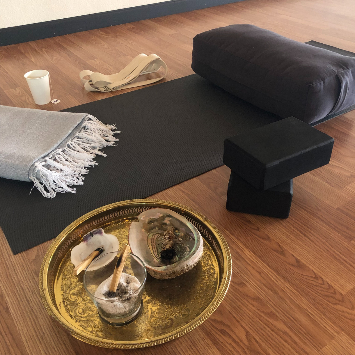 Yoga mat setup with bolster, blocks, blanket, and ceremonial tray used for grounding rituals.