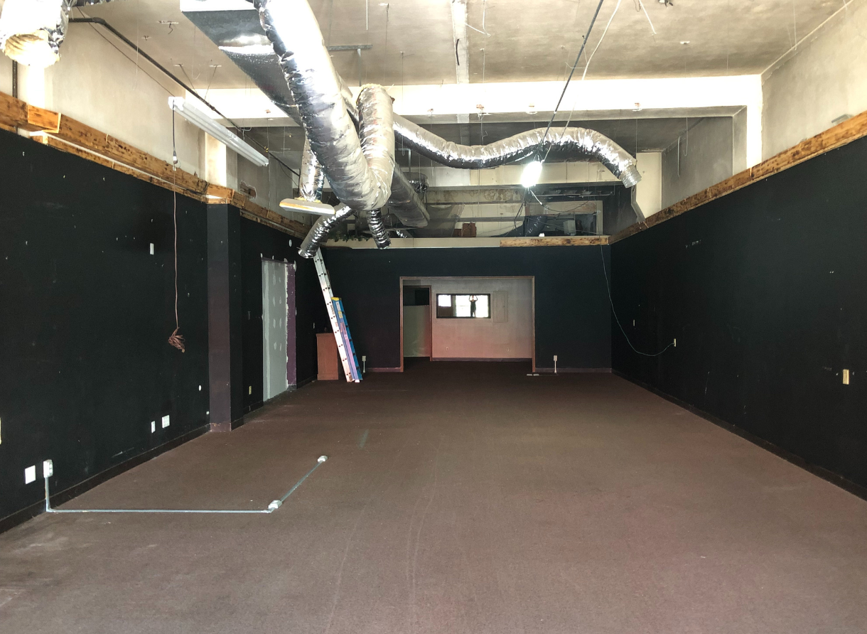 Empty commercial space before renovation with exposed ductwork and unfinished walls.