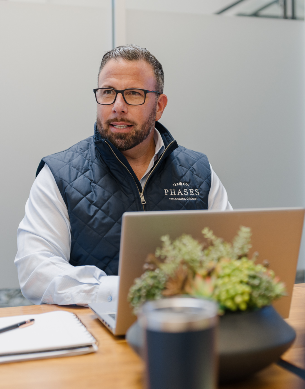 A Phases Financial Group advisor working at a laptop in a conference room, wearing a branded vest.