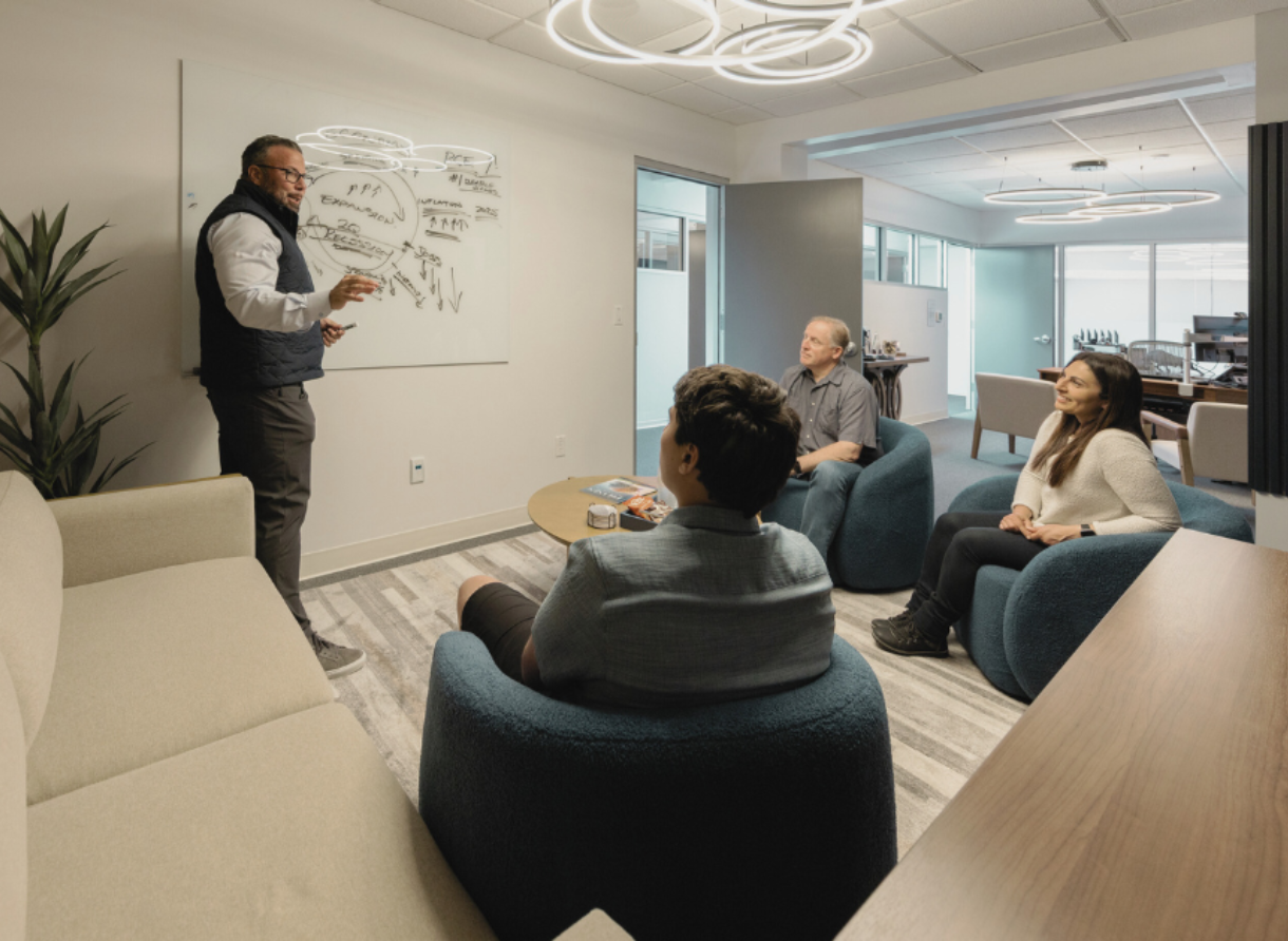 A Phases Financial Group advisor presenting at a whiteboard while clients listen during a collaborative meeting in a modern office lounge.
