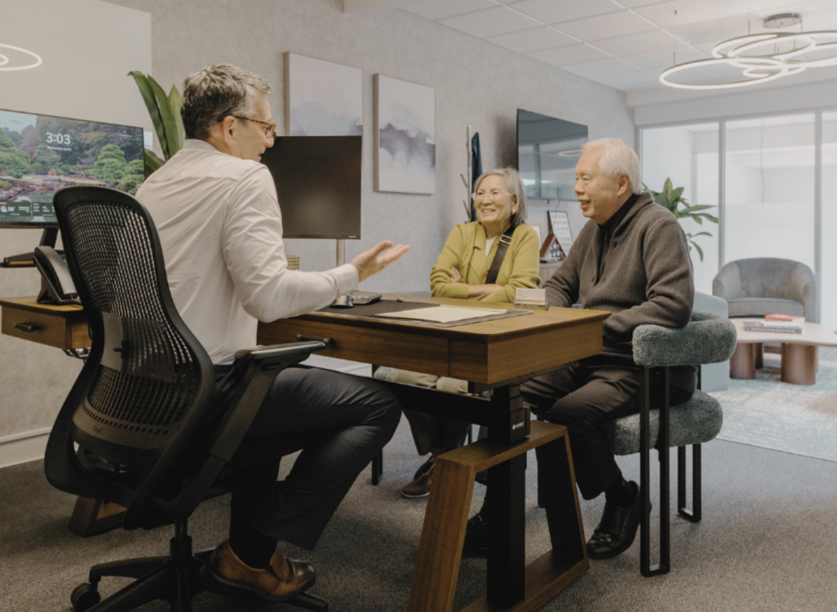 A Phases Financial Group advisor meeting with two clients at a desk in a private office setting.
