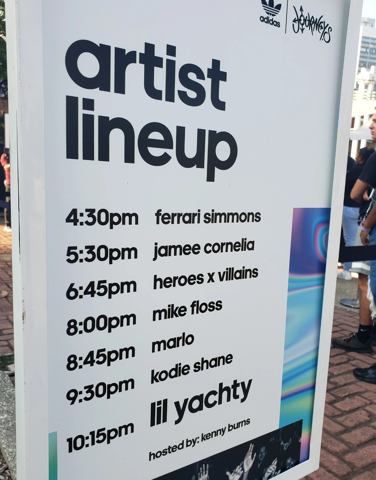 Freestanding event sign displaying the artist lineup and performance times for an adidas and Journeys outdoor music experience, featuring Ferrari Simmons, Jamee Cornelia, Heroes x Villains, Mike Floss, Marlo, Kodie Shane, and Lil Yachty.