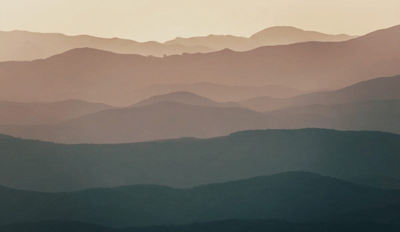 Layered mountain ridges recede toward the horizon in soft, muted tones, creating a sense of depth and expansive perspective.